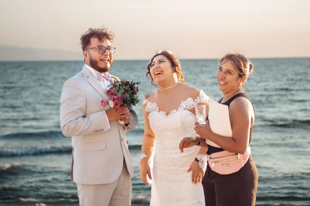 Novios sonriendo junto al mar con una acompañante
